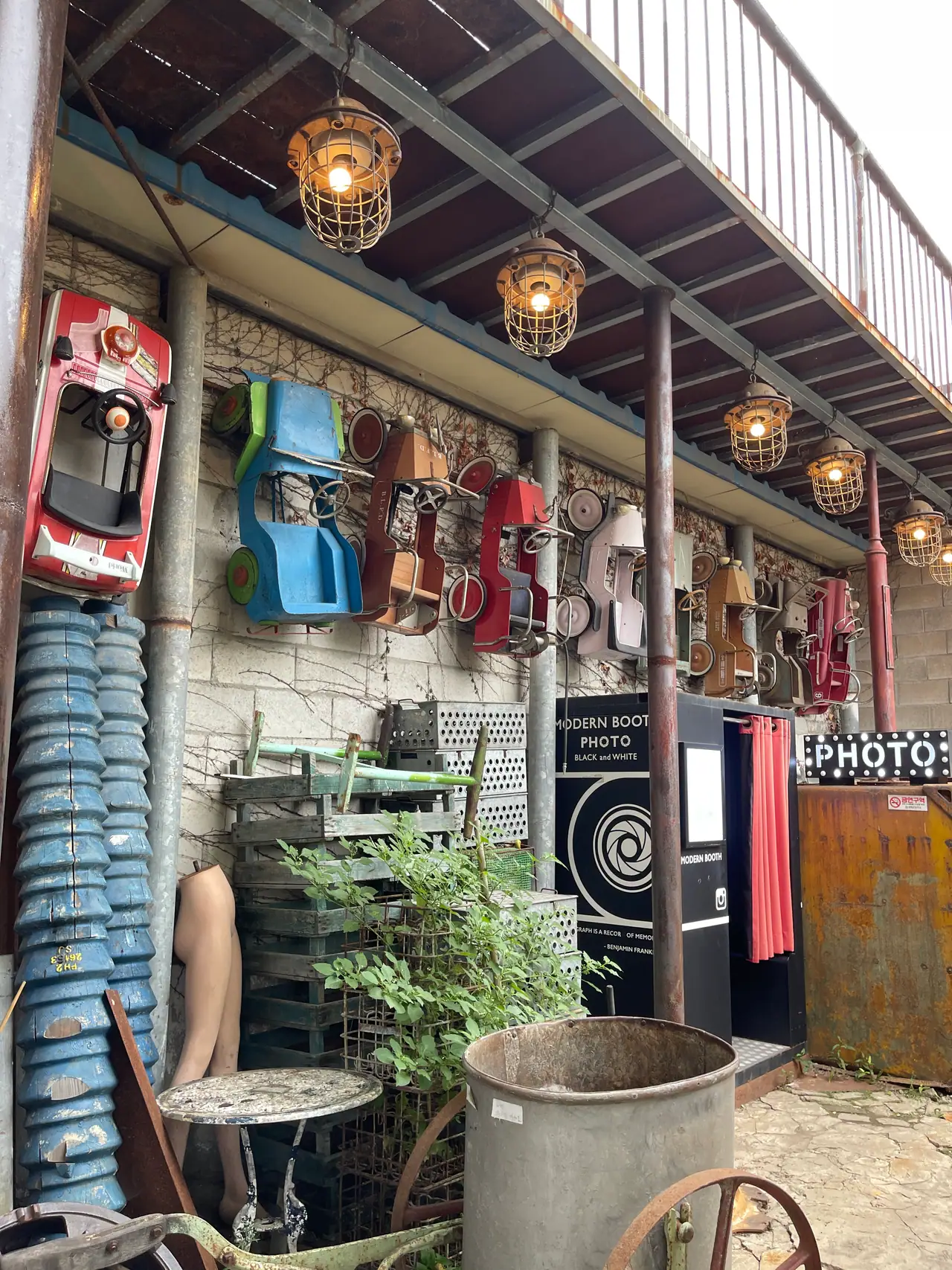 A shop front of salvaged objects — sandals and boards hung on a stone wall beneath a balcony strung with bare bulbs.