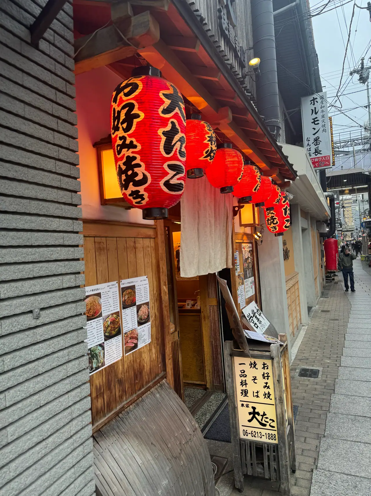 Red paper lanterns and a menu board hang outside a wooden restaurant front.