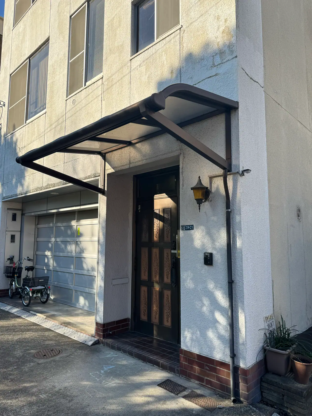 A dark awning and a wall lamp mark the doorway of a plain white building.