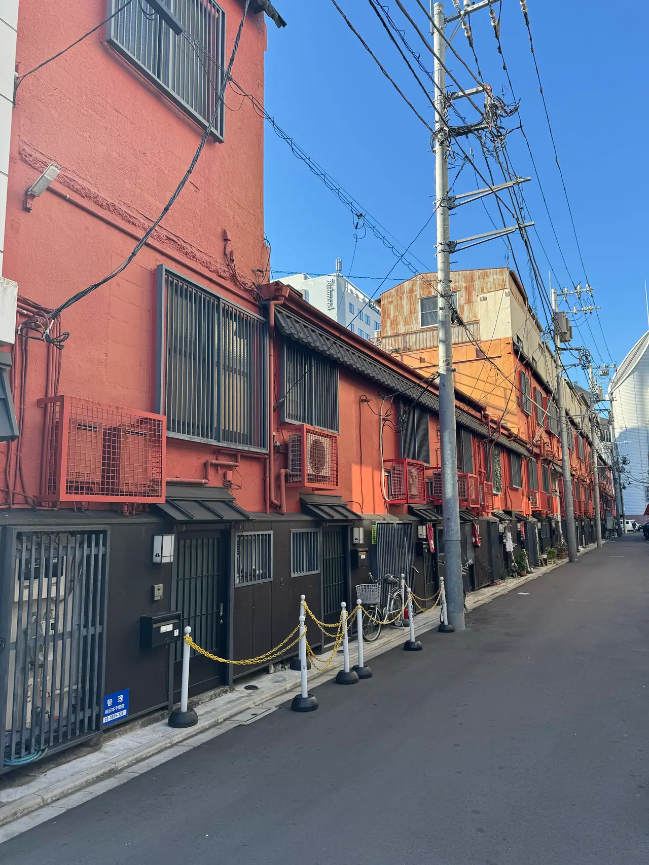 A row of red-painted shopfronts runs to a vanishing point beneath a web of power lines.