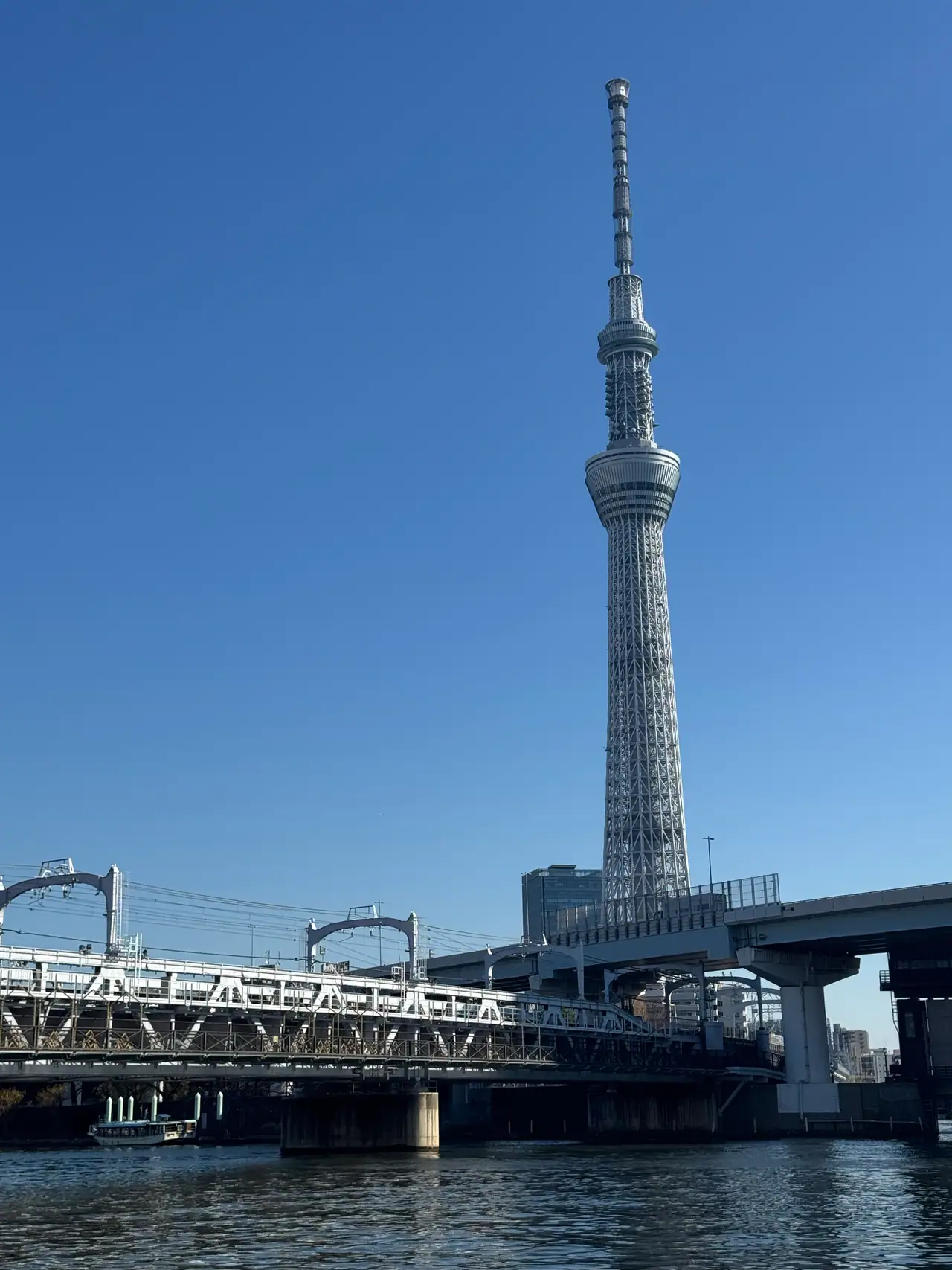 The Skytree rises above a steel bridge and an elevated road under a cloudless sky.
