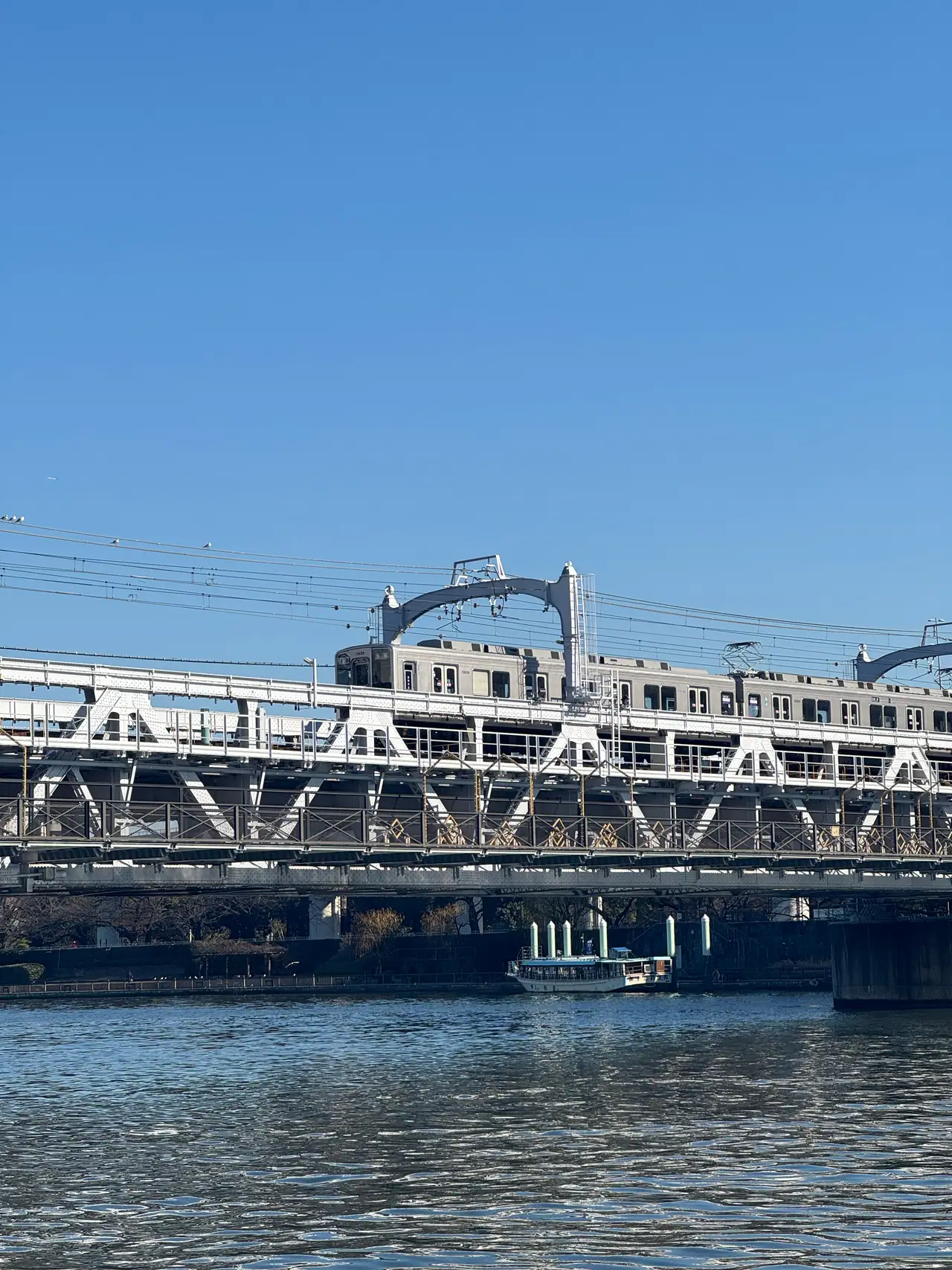 A train crosses a white steel truss bridge over the river, a boat moored below.