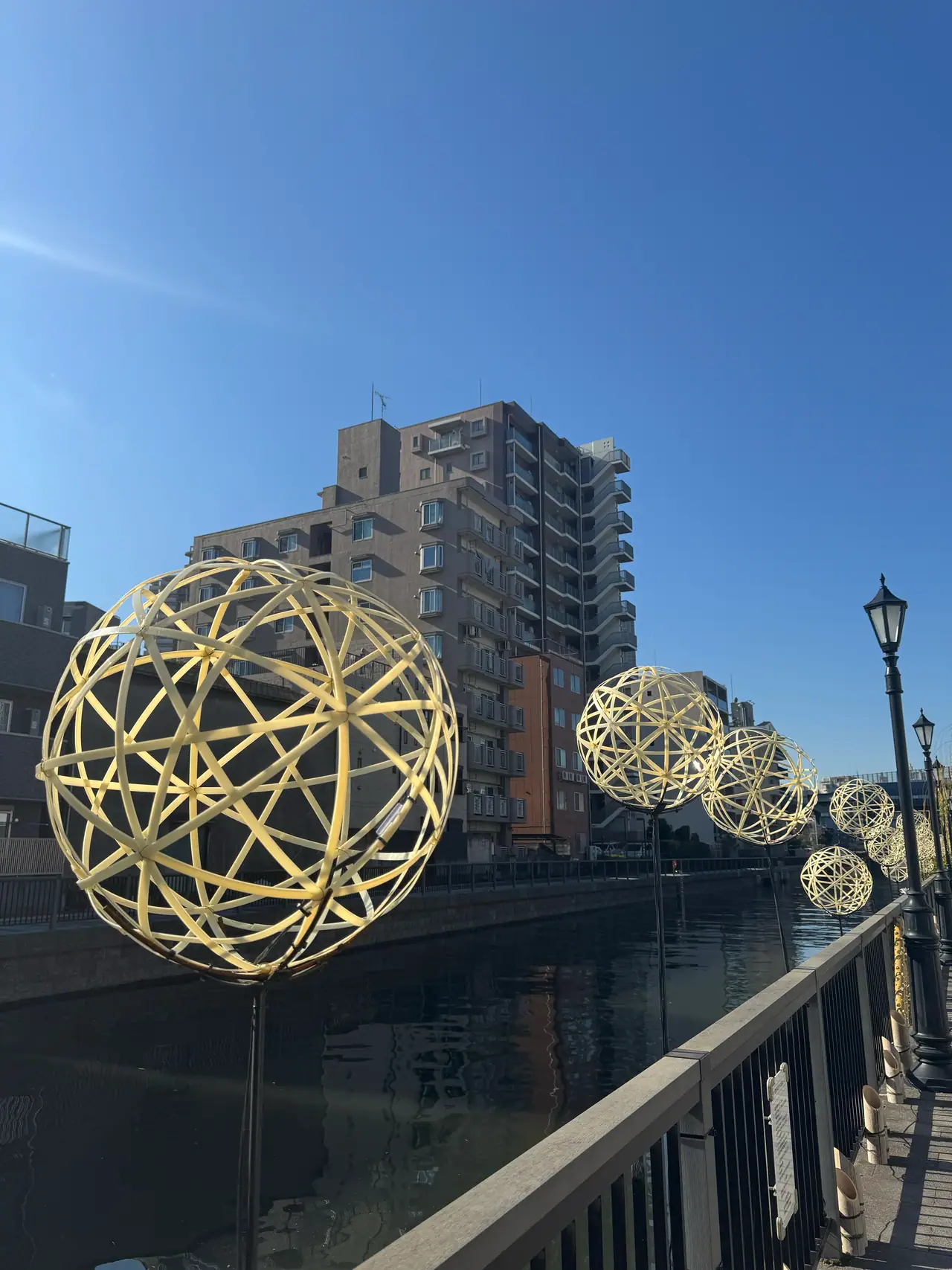 Gilded wire spheres sit along a riverside railing in front of an apartment block.