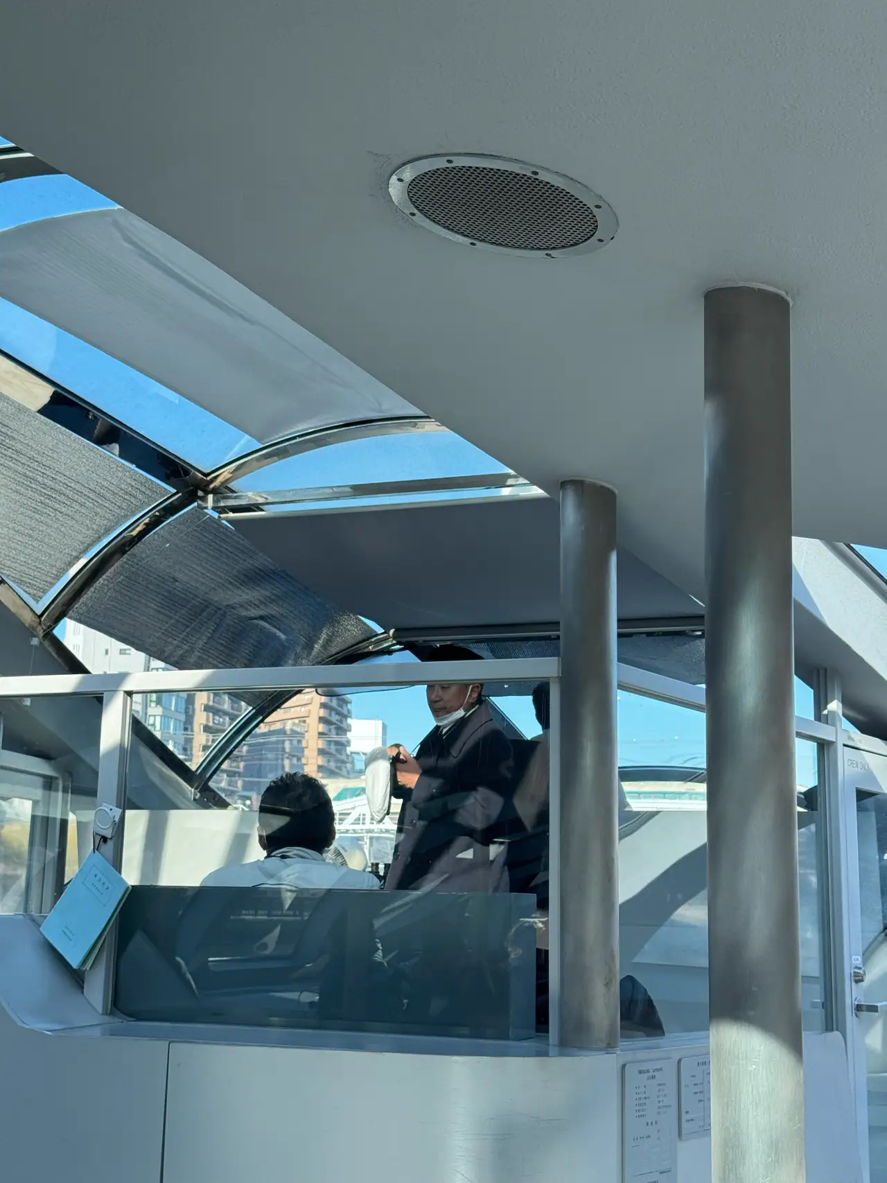 Inside a glass-roofed water bus, the pilot stands at the helm behind curved windows.