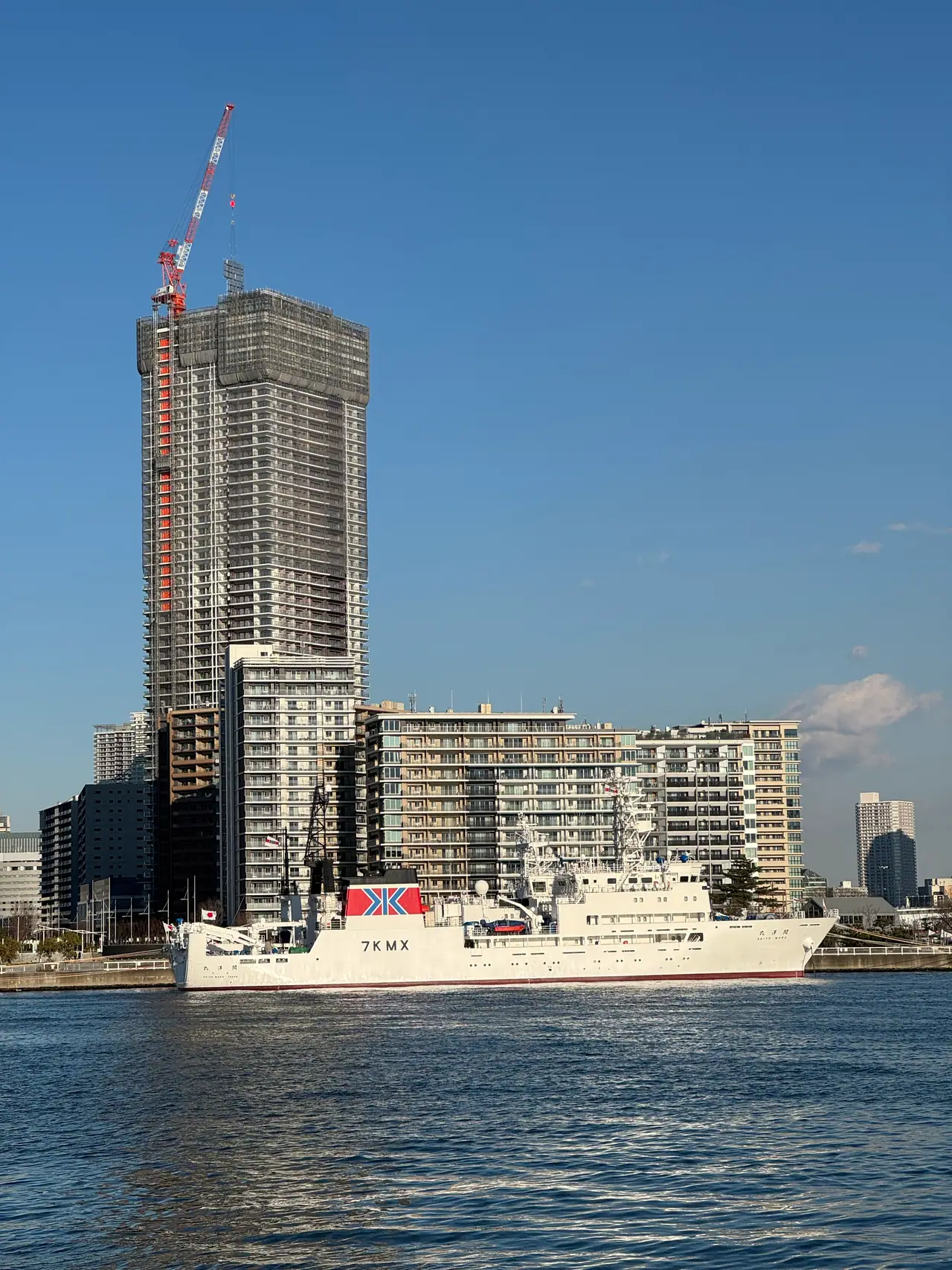 A white ship lies at a wharf below apartment towers, one still under construction with a crane on top.