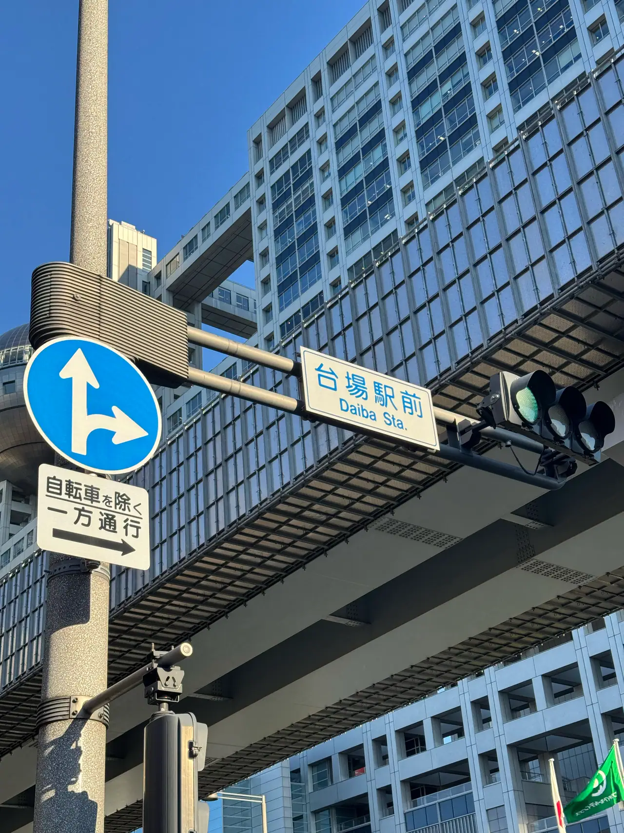 Blue direction signs and a station nameplate hang from a pole beneath an elevated railway.