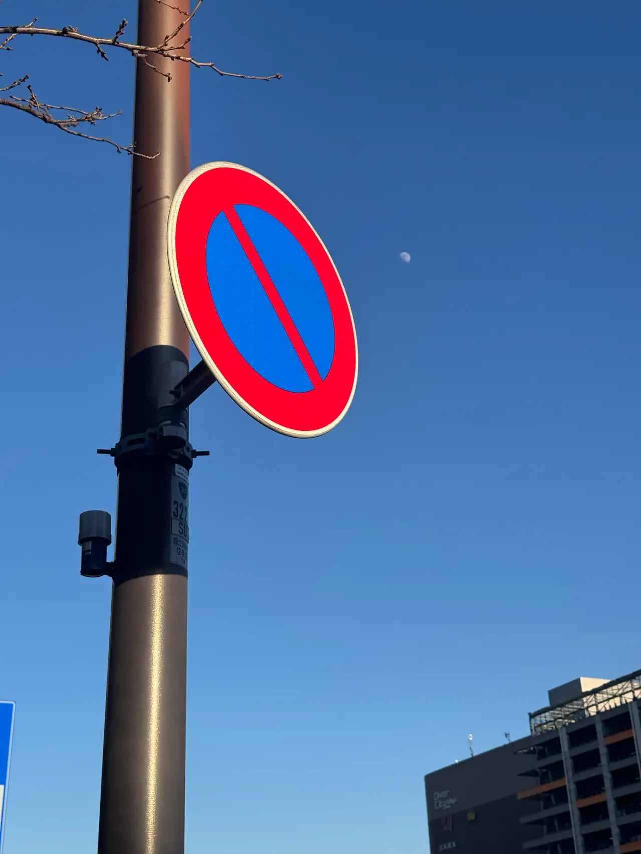 A blue and red no-parking sign faces the sky, a pale half moon hanging just beyond it.