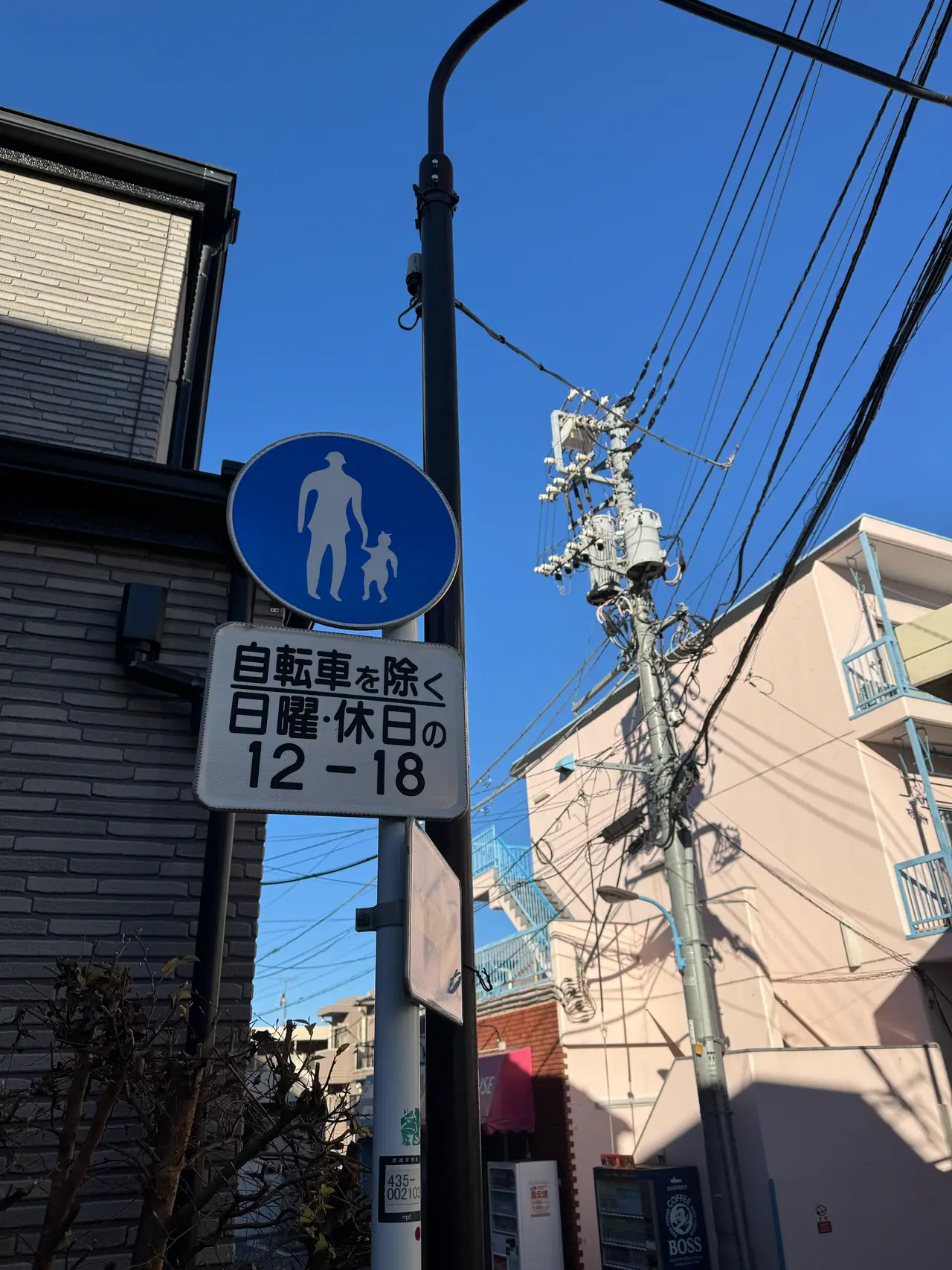 A blue pedestrian sign lists permitted hours beneath a knot of power lines and transformers.