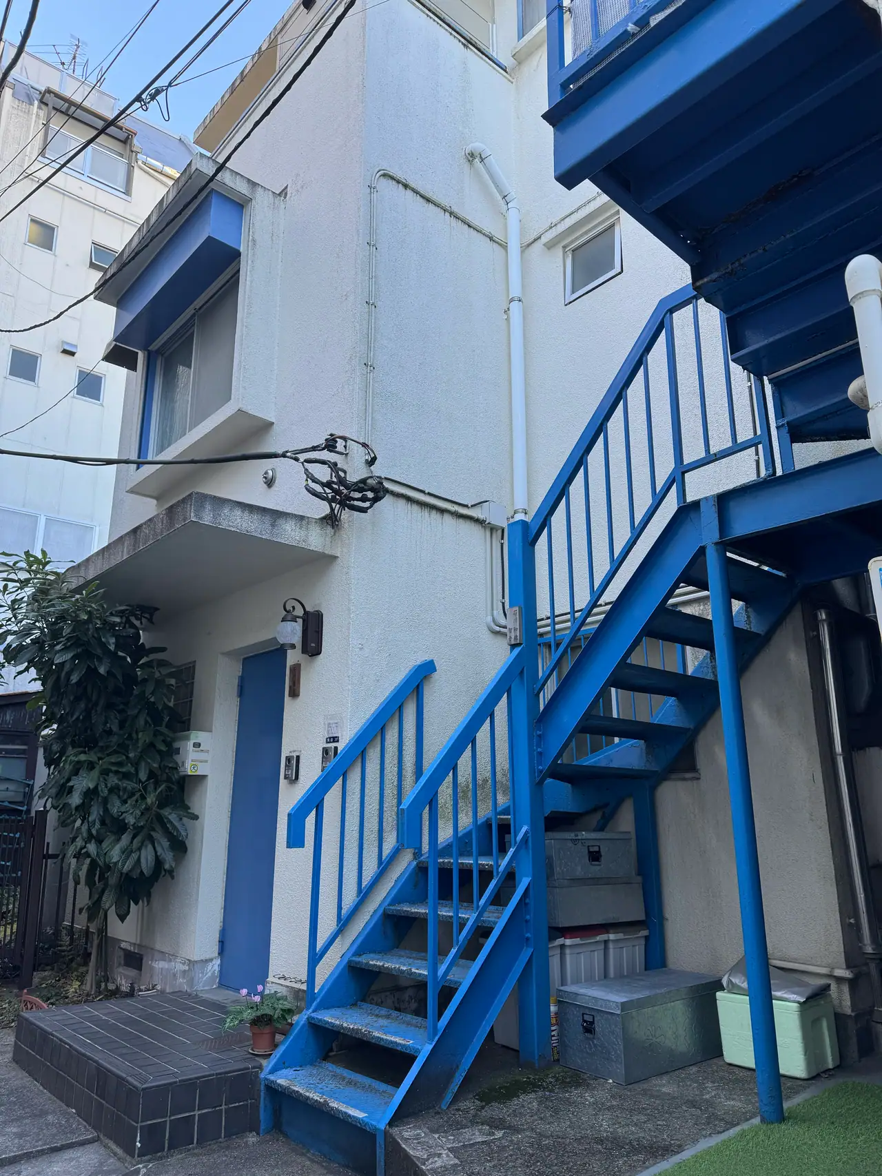A blue steel staircase and railing climb the outside of a white building.