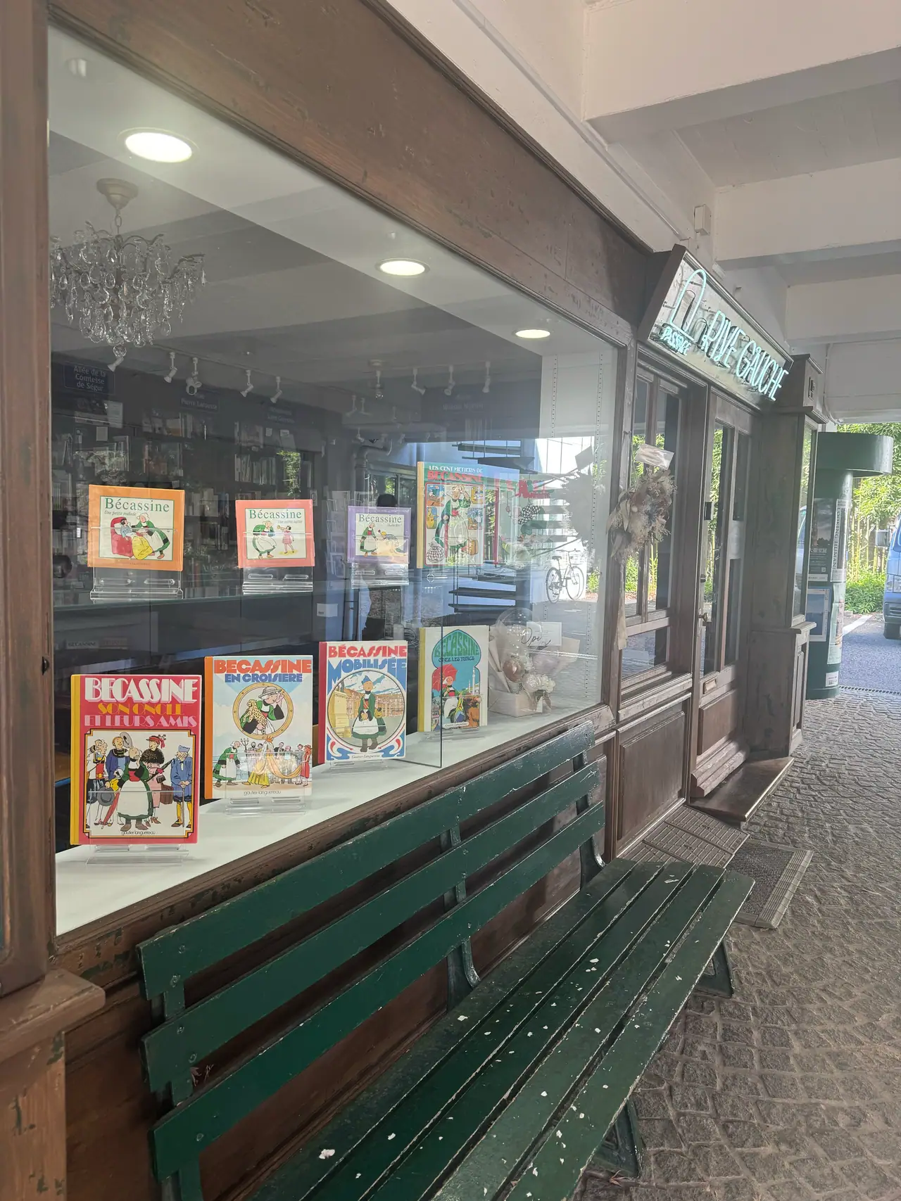 Old illustrated books stand in a shop window above a weathered green bench.