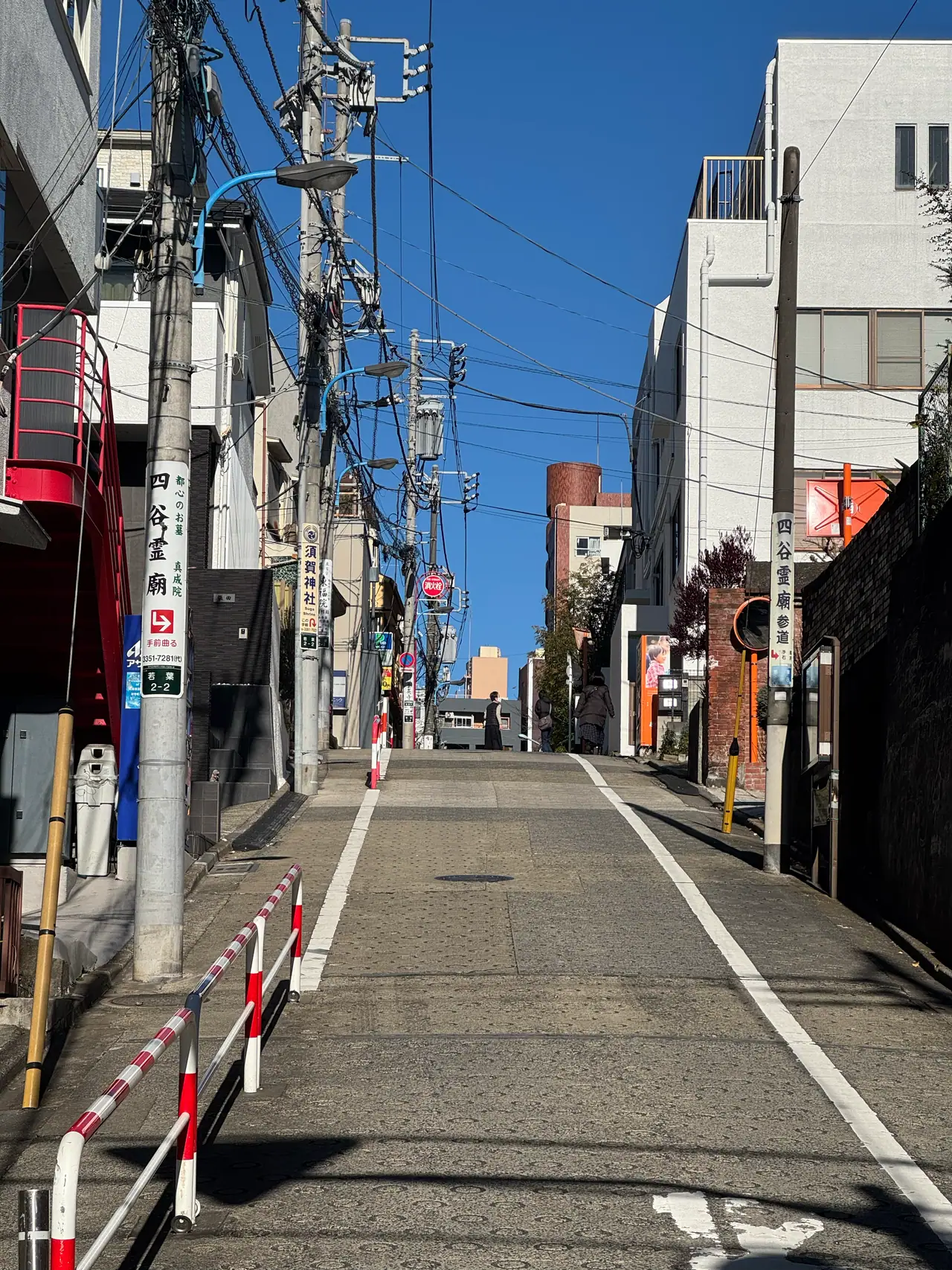 Power poles line both sides of a narrow street running straight to a distant crossing.
