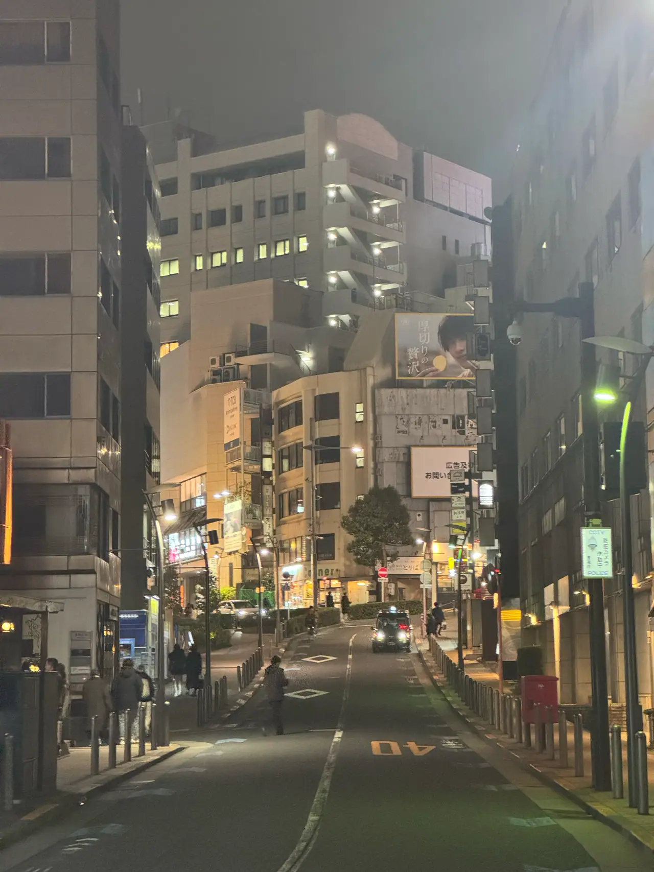 A quiet street slopes downhill between lit apartment blocks at night.