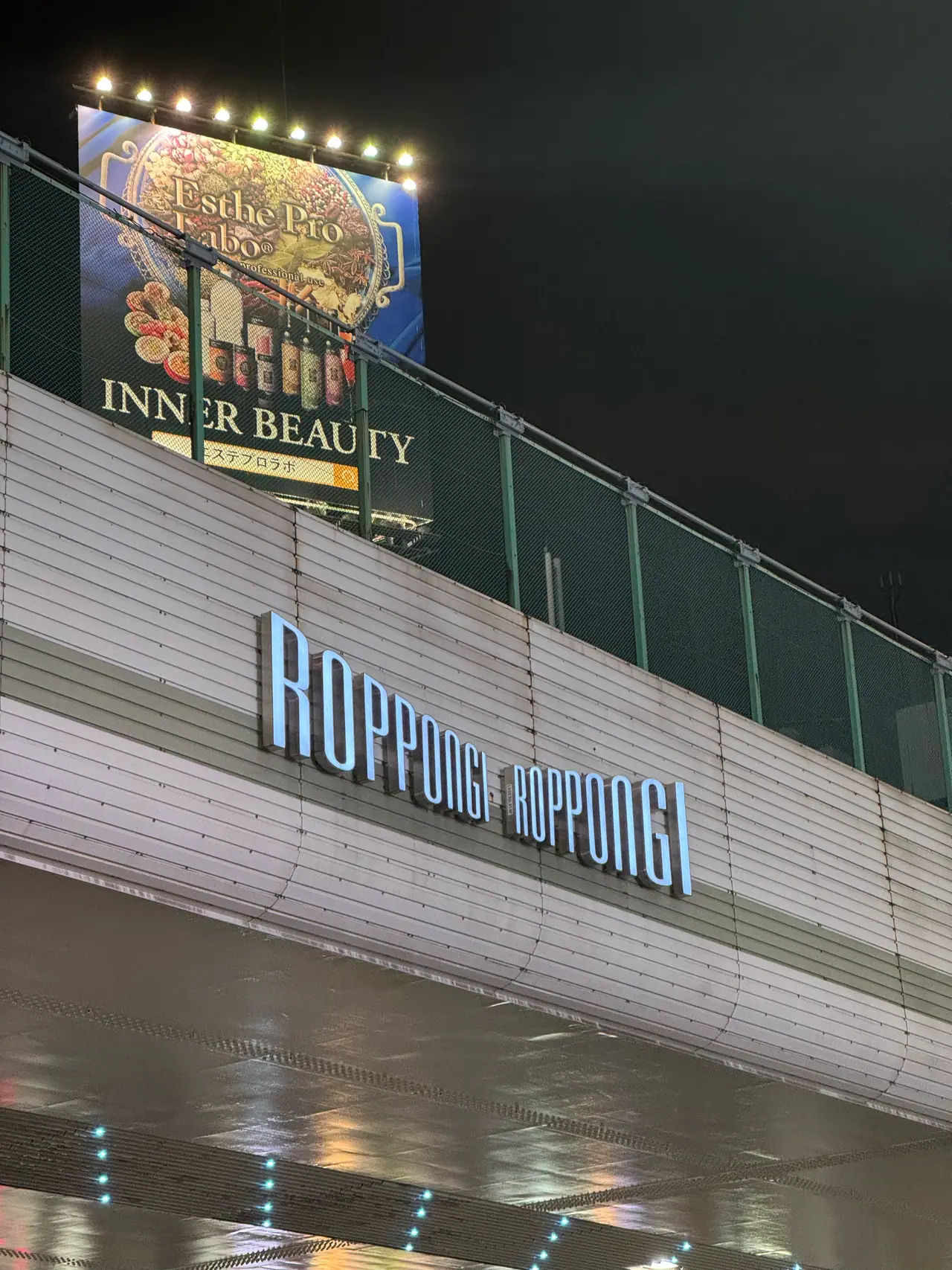 The word Roppongi runs twice along an elevated walkway above a wet, reflecting deck.