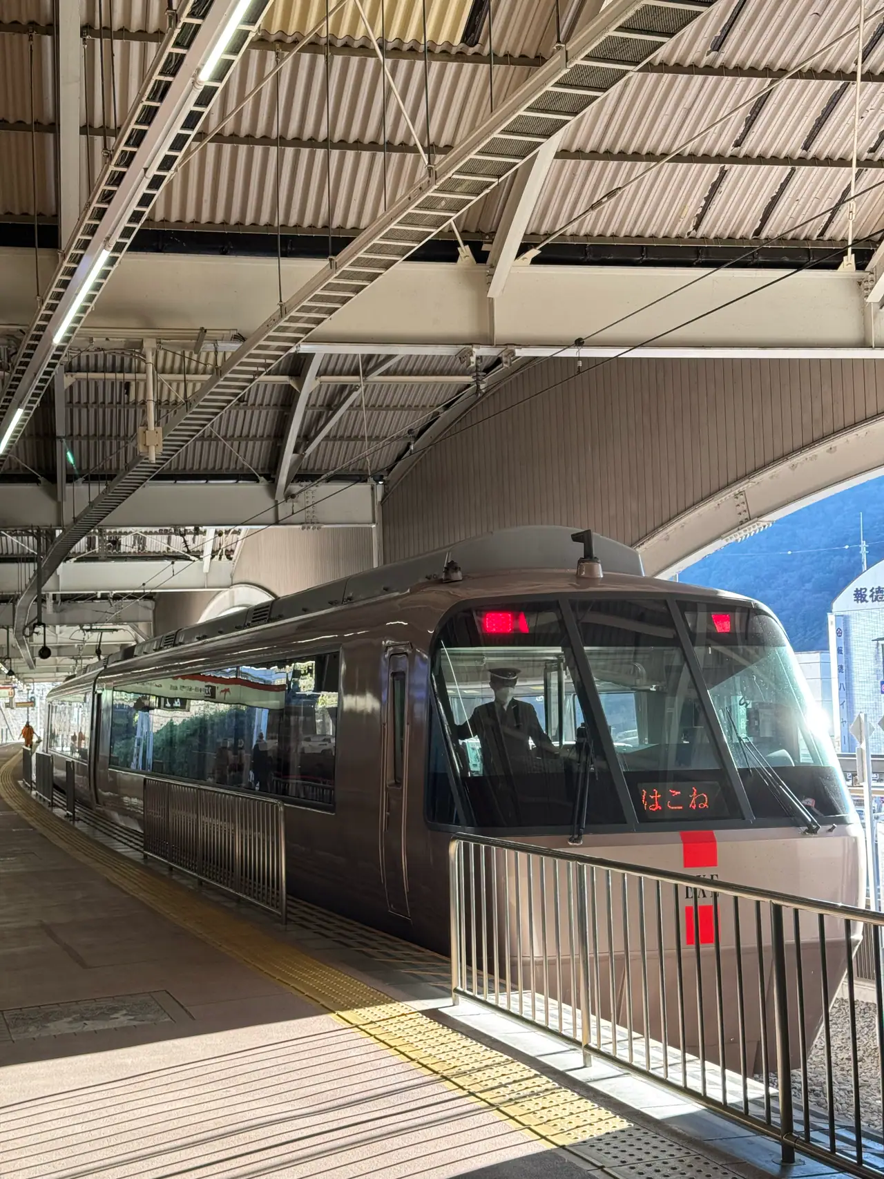 The nose of a Romancecar bound for Hakone waits under a curved platform canopy.