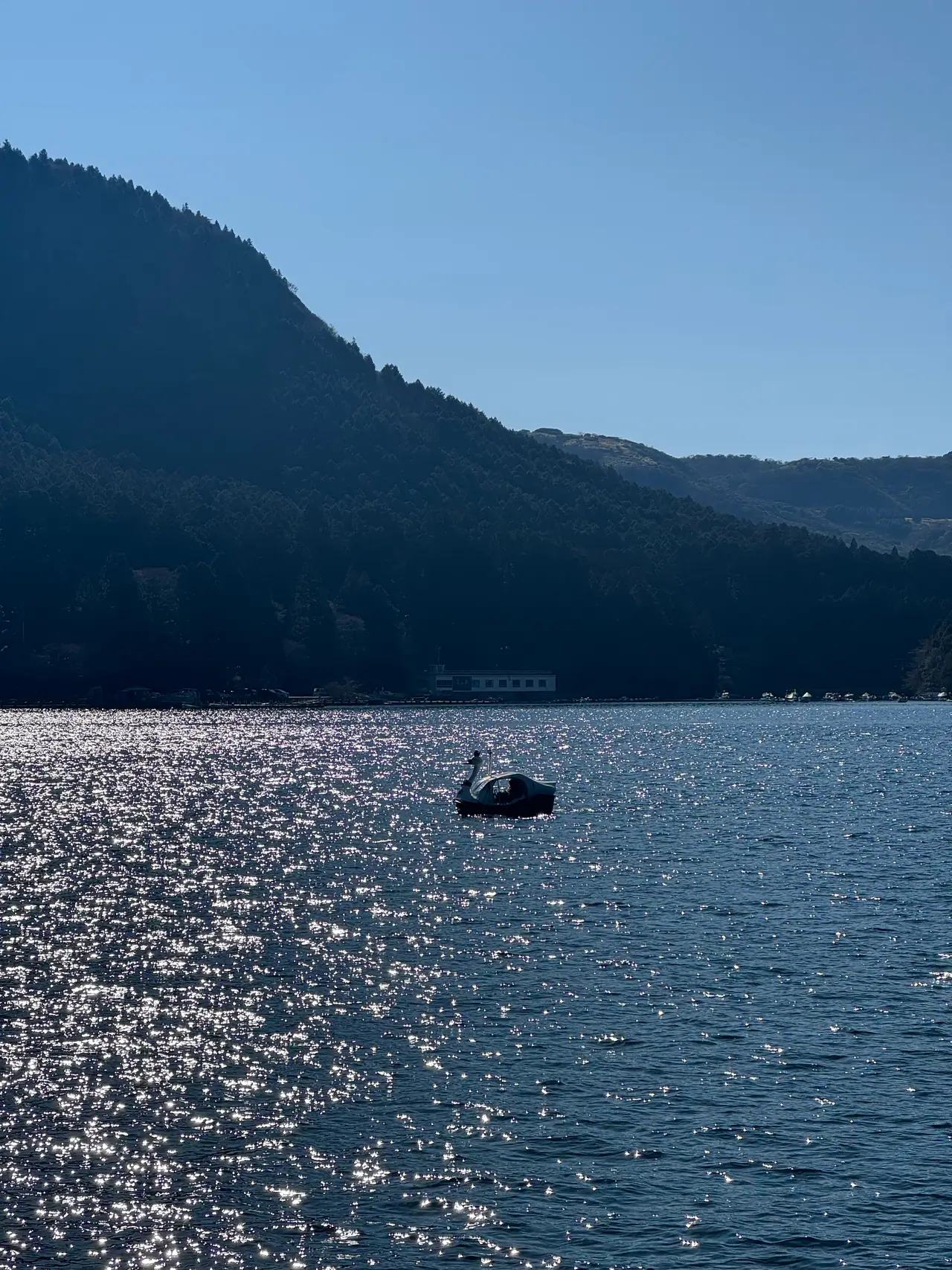 A single small boat sits on a lake of broken light below a dark forested ridge.