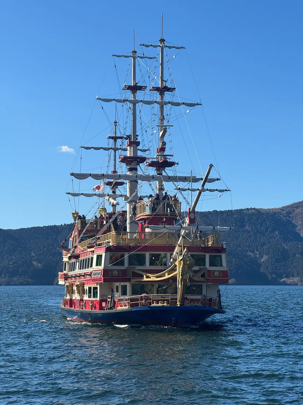 A replica galleon crosses the lake in front of forested mountains.