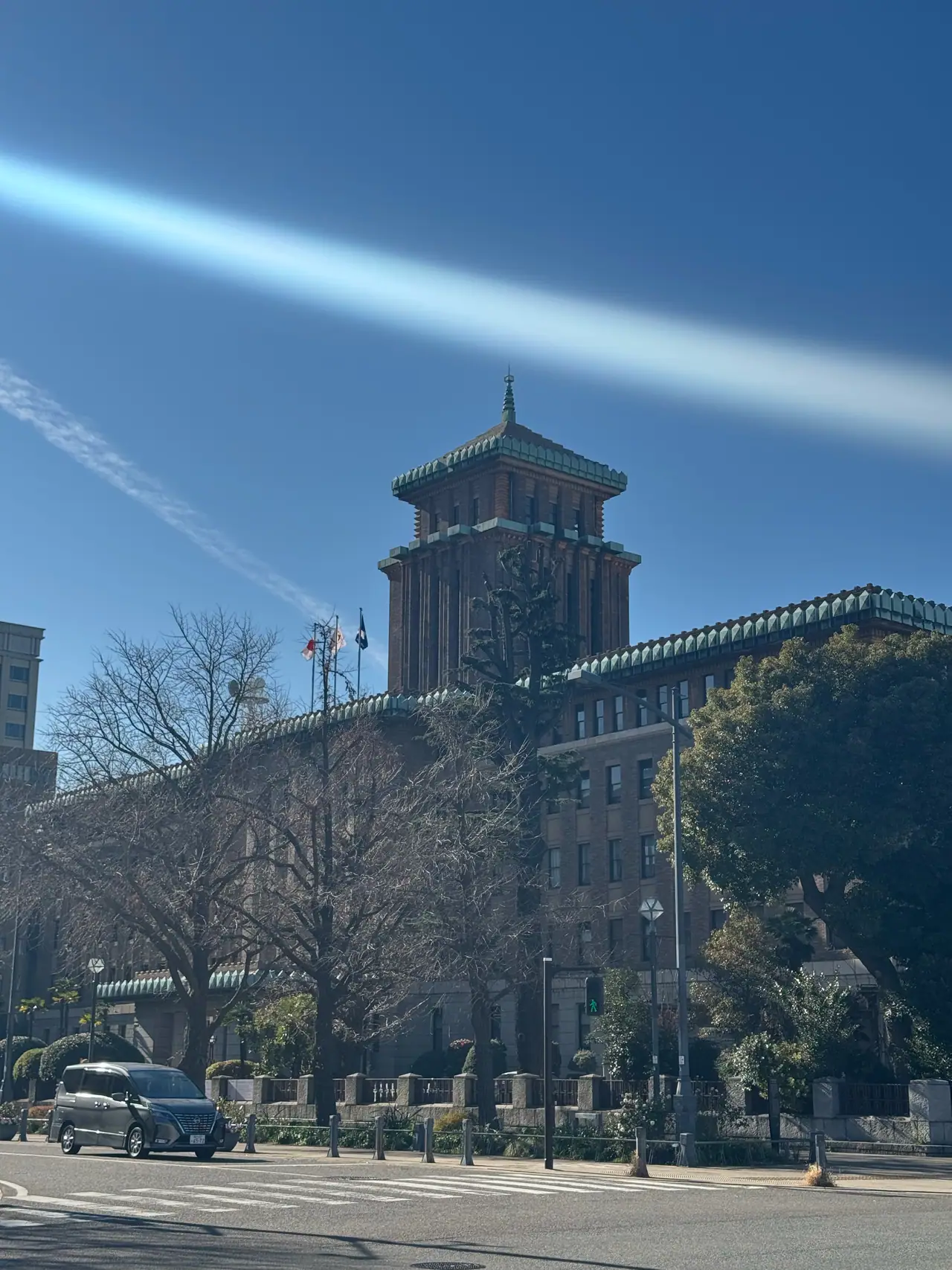 Two contrails cut diagonally across the sky above the tower of the prefectural office.