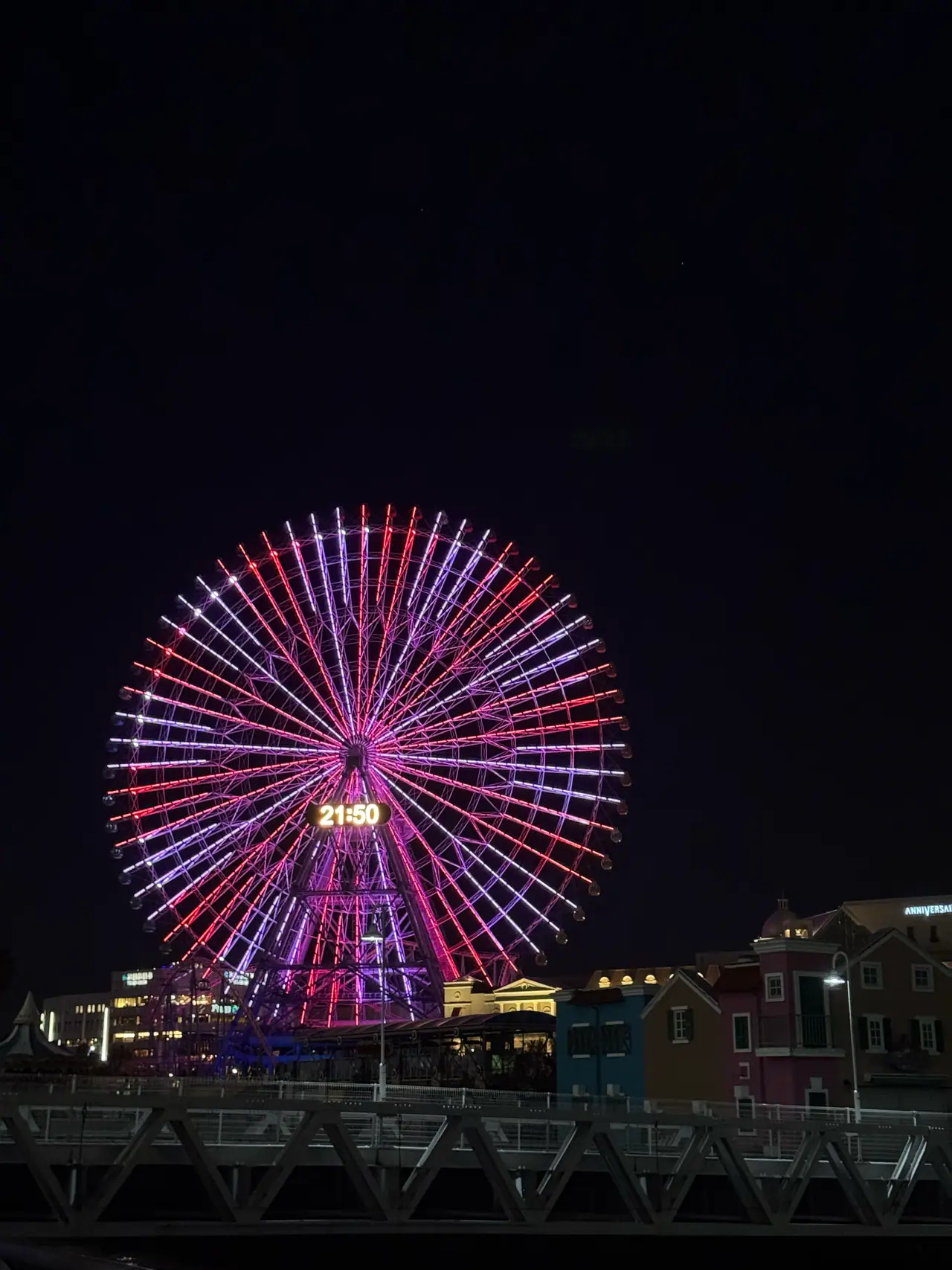 The same ferris wheel glows pink and violet against a black sky, reading 21:50.